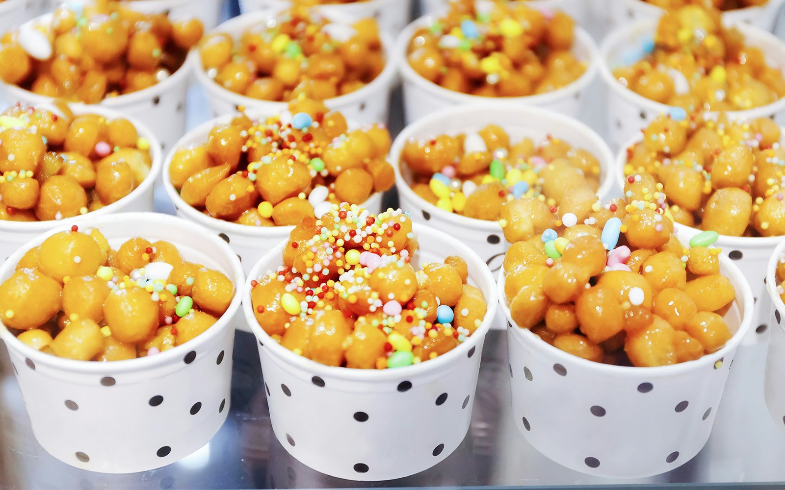 Struffoli in polka dot cups, topped with colorful sprinkles, a traditional Neapolitan pastry.