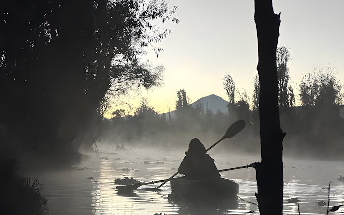 Kayaker paddling at sunrise in the misty canals of Xochimilco.