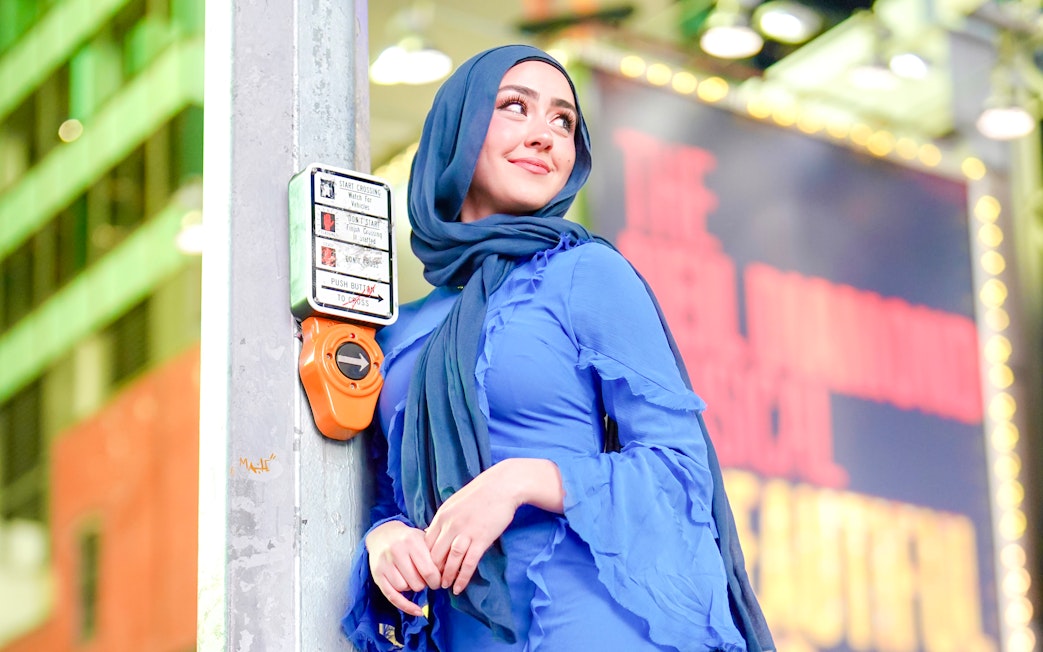 Person leaning on a crosswalk button in Times Square, NYC.