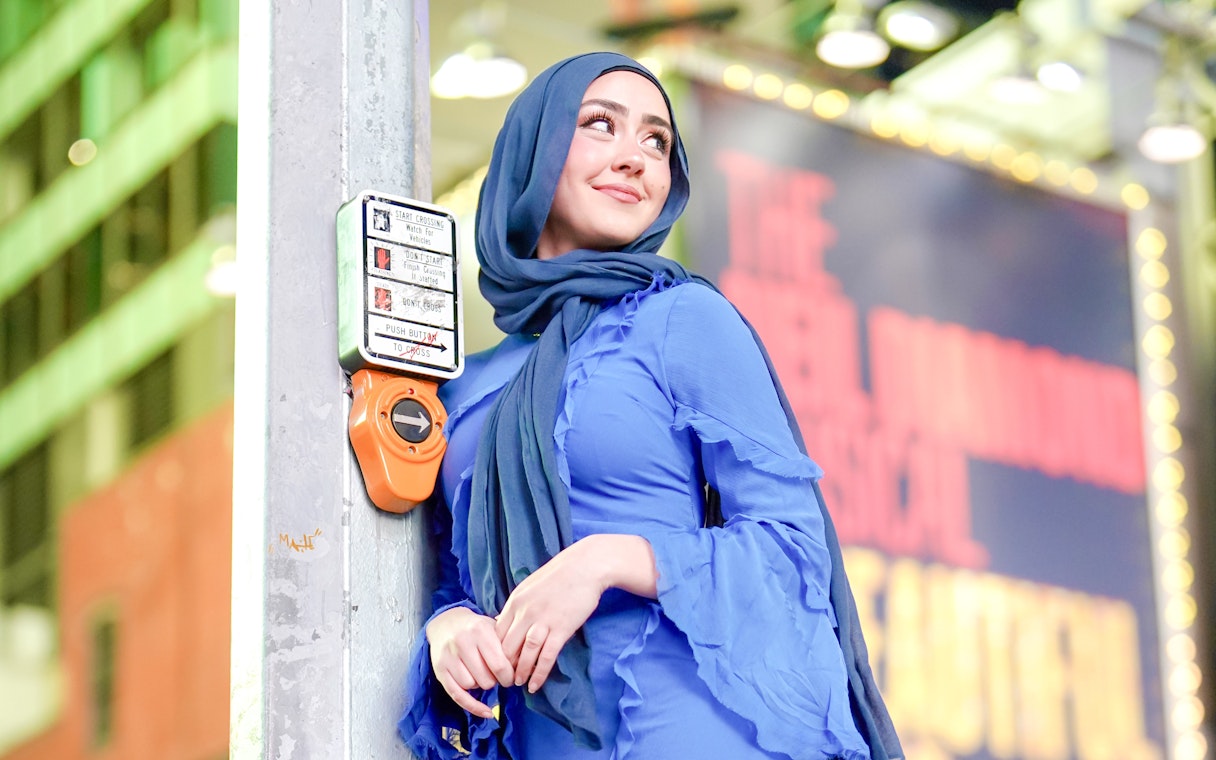 Person leaning on a crosswalk button in Times Square, NYC.