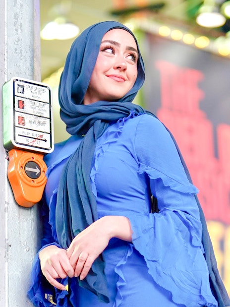 Person leaning on a crosswalk button in Times Square, NYC.