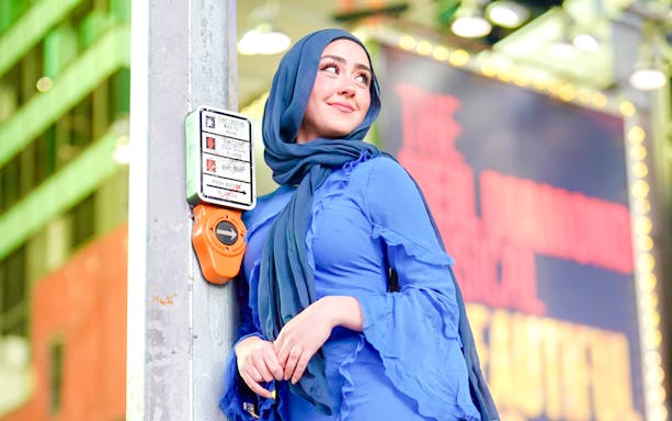 Person leaning on a crosswalk button in Times Square, NYC.