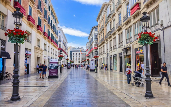 Pedestrian street in Malaga with shops and people, part of self-guided city exploration game.