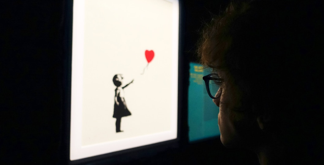 Visitor viewing Banksy's girl with balloon artwork.