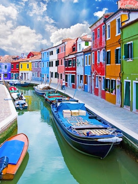 Colorful buildings along a canal with boats in Burano, Italy.