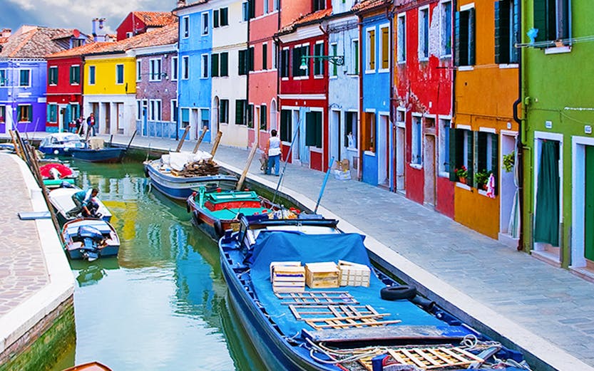 Colorful buildings along a canal with boats in Burano, Italy.