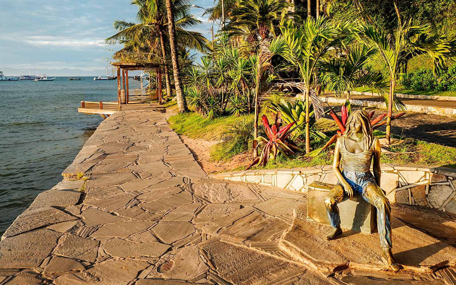 Sidewalk along Canto Beach in Buzios, Brazil with a bronze statue and ocean view.