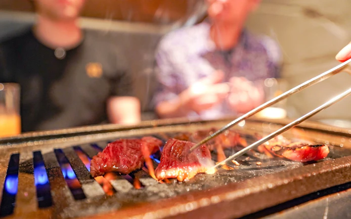 Grilling A5 Wagyu beef on a hot plate during Tokyo Omakase Sushi & Foodie Tour in Shinjuku.