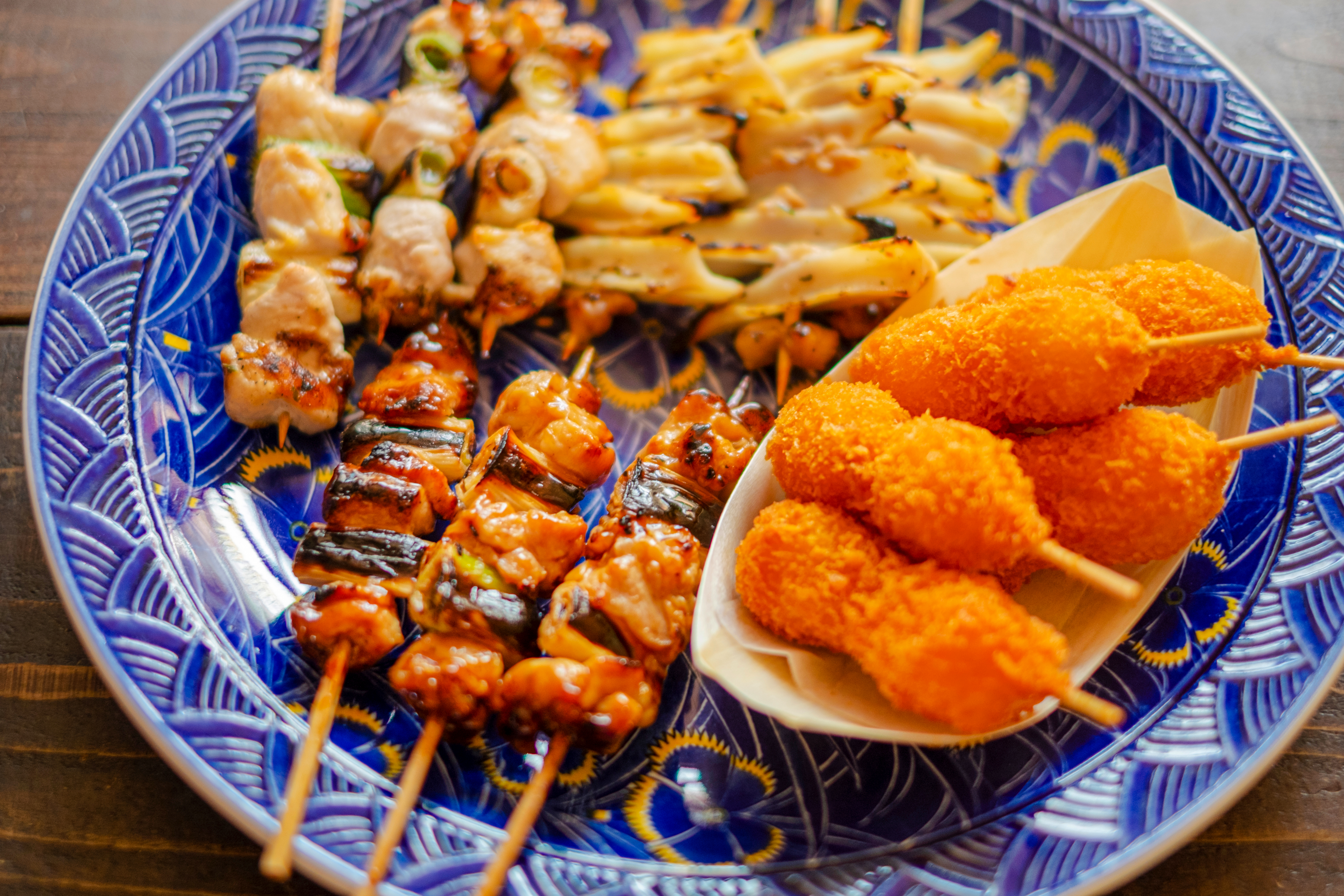 Kushikatsu platter with assorted skewers on a decorative blue plate.