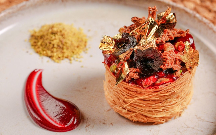 Kataifi dessert with gold leaf and berry garnish at The Nomad Garden, Arabian desert dining experience.