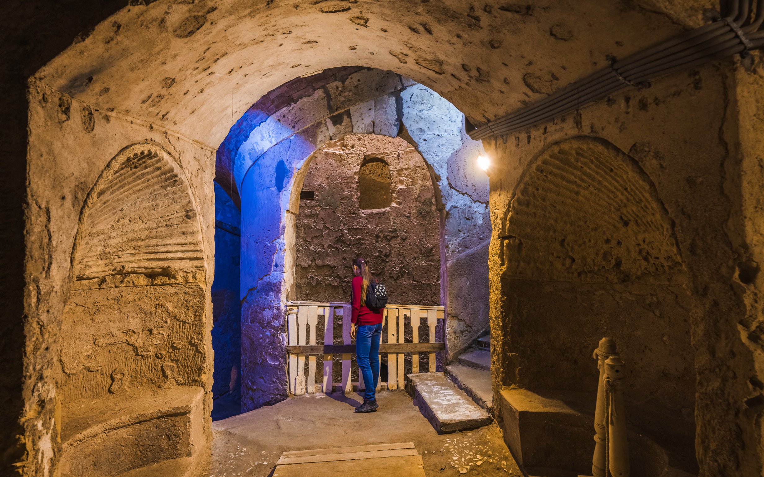 Visitor exploring the ancient catacombs of Alexandria with stone arches and dim lighting.