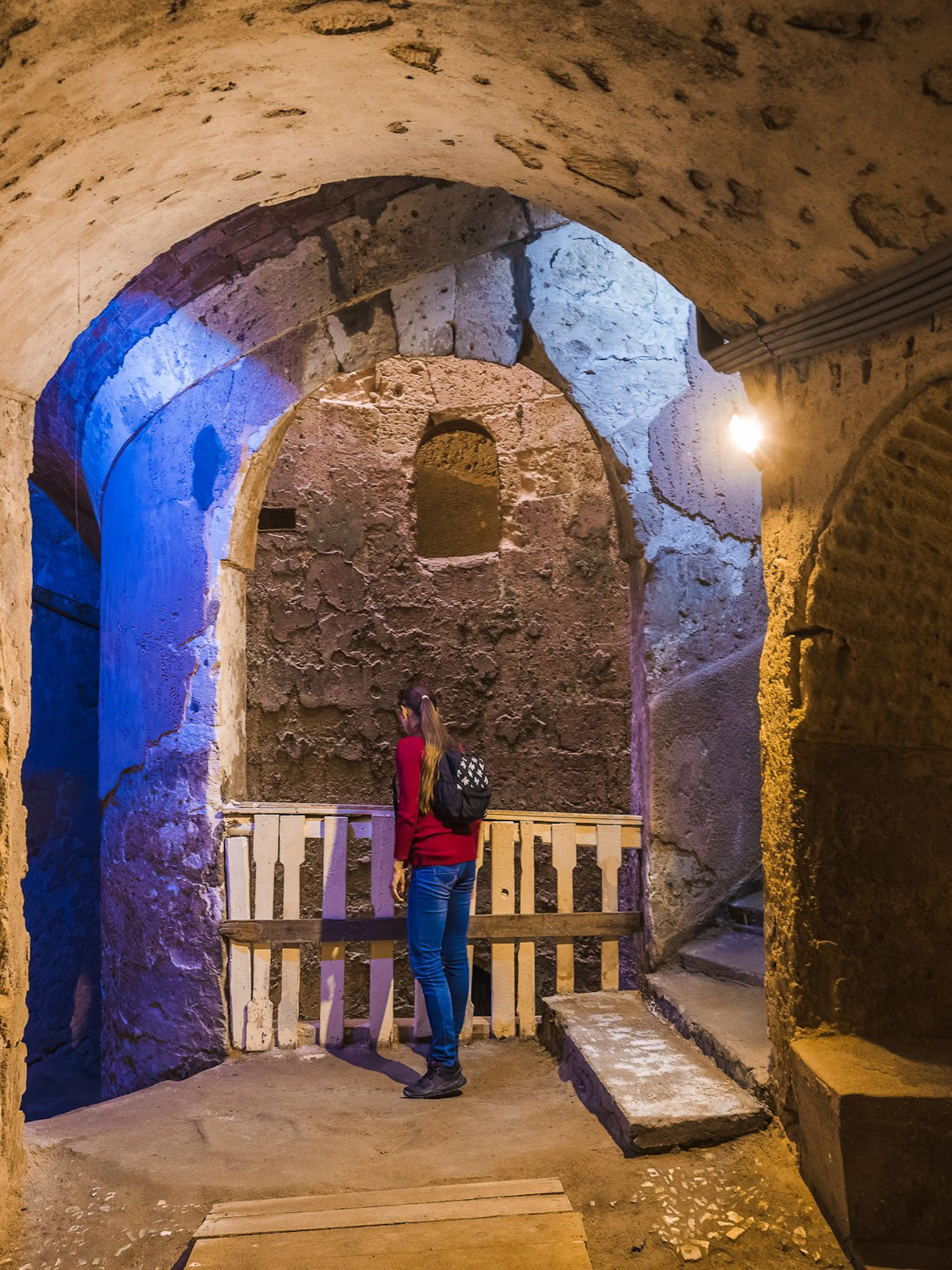 Visitor exploring the ancient catacombs of Alexandria with stone arches and dim lighting.