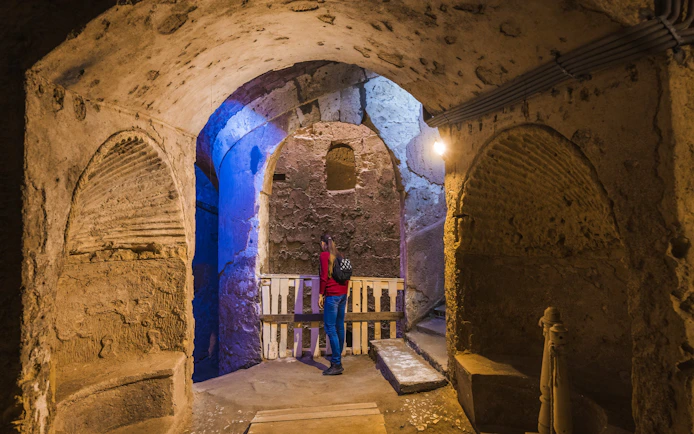 Visitor exploring the ancient catacombs of Alexandria with stone arches and dim lighting.