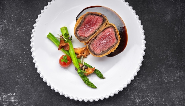Beef Wellington served on a white plate with side salad like tomatoes and lettuce