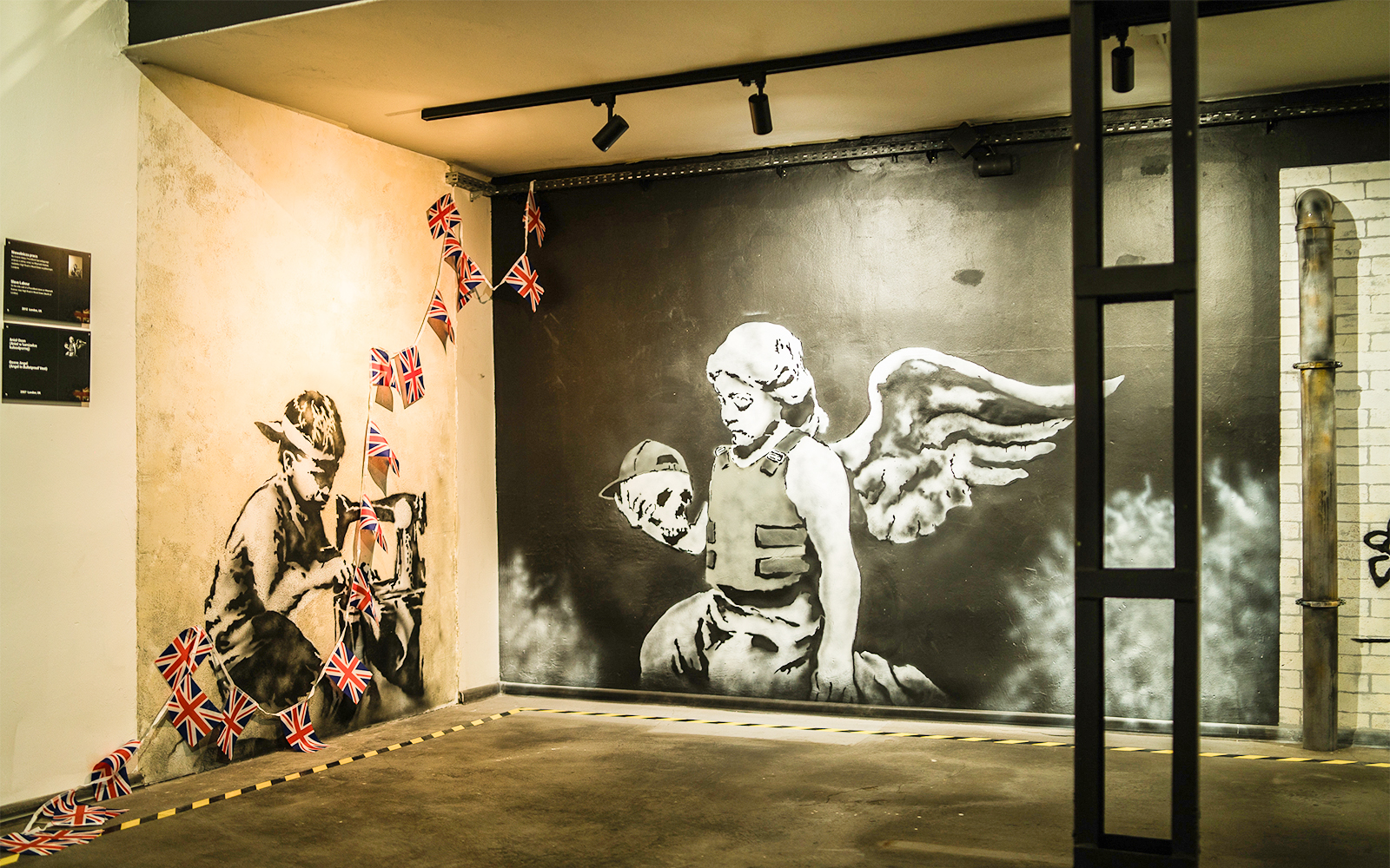 Street art of a child sewing Union Jack flags and an angel with a skull at Banksy Museum, Krakow.