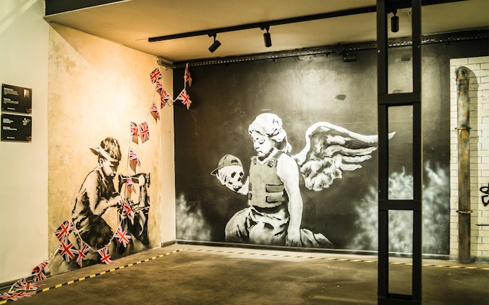 Street art of a child sewing Union Jack flags and an angel with a skull at Banksy Museum, Krakow.