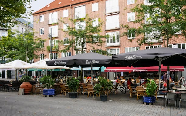 Outdoor cafes in St. Georg, Hamburg, with people dining under umbrellas.