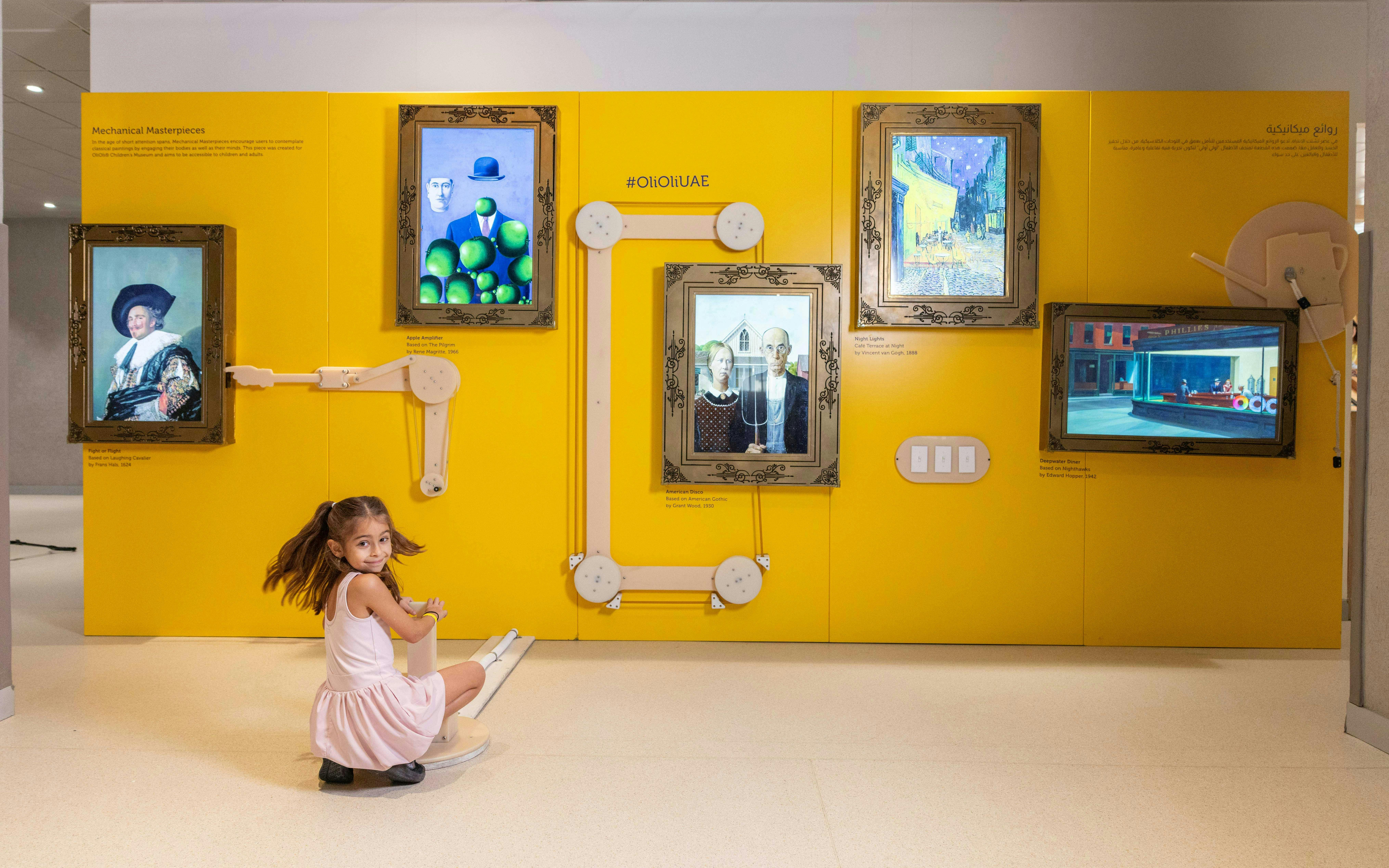 Child interacting with art exhibit at OliOli Children's Museum, featuring famous paintings on a yellow wall.