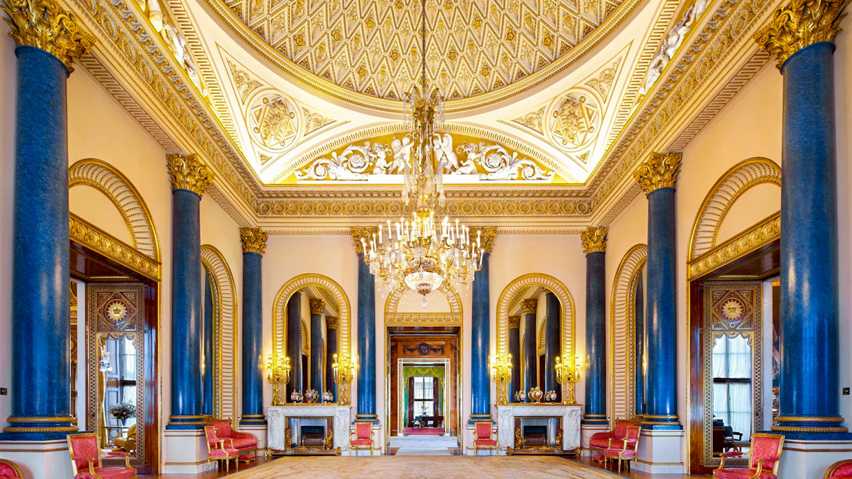 Buckingham Palace interior with ornate ceiling, chandeliers, and blue columns.