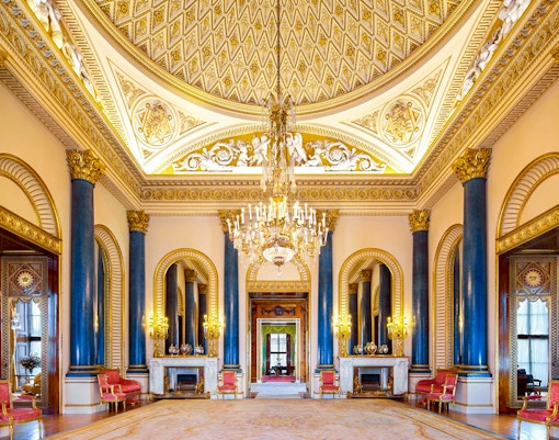 Buckingham Palace interior with ornate ceiling, chandeliers, and blue columns.