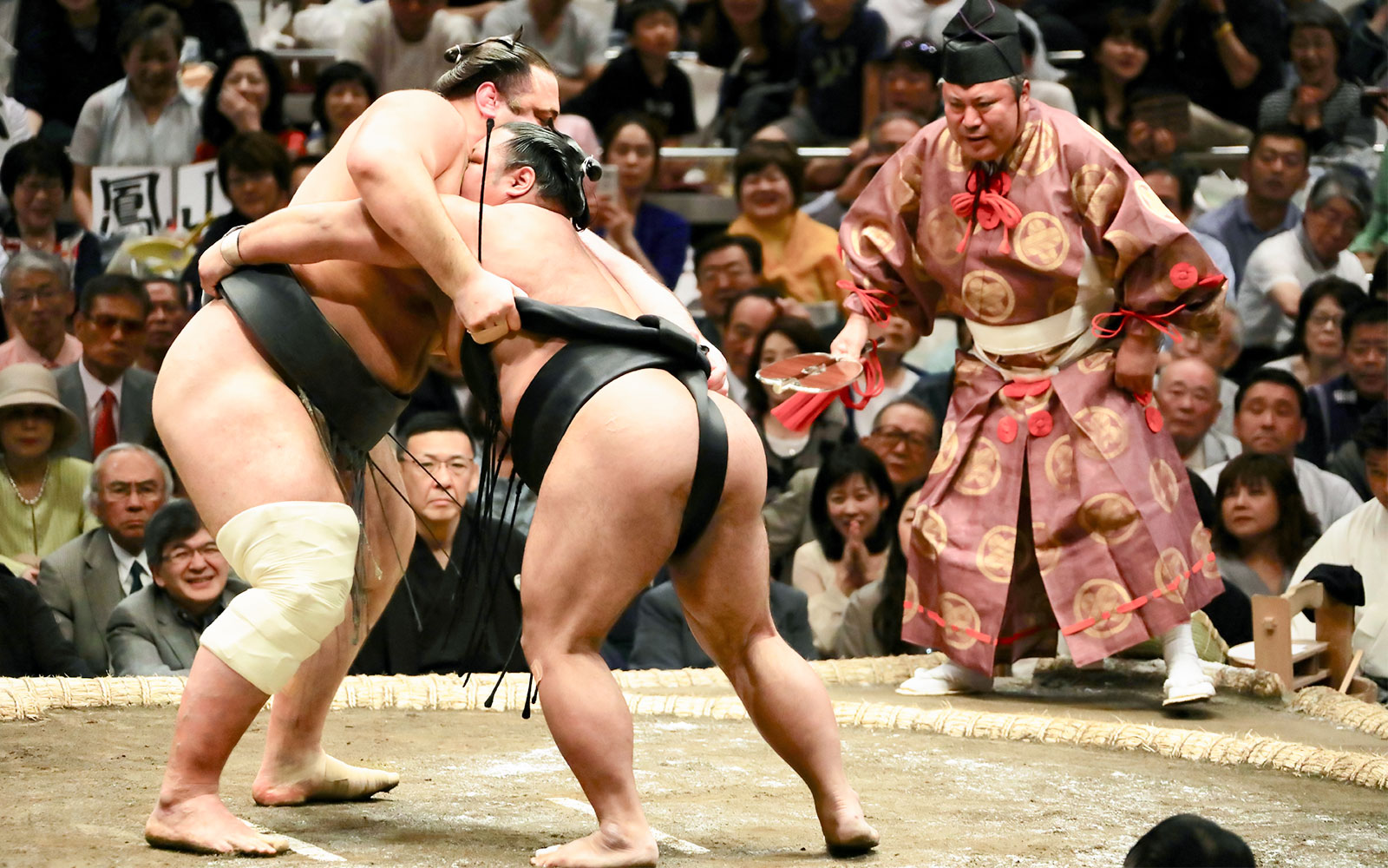 Sumo wrestlers competing in a Tokyo tournament with a referee observing.