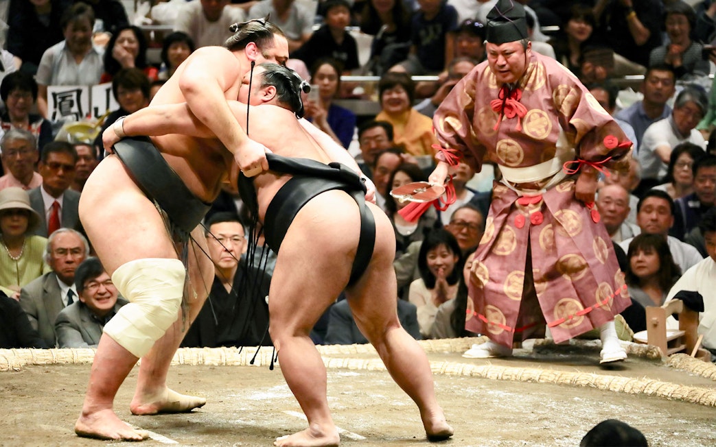 Sumo wrestlers competing in a Tokyo tournament with a referee observing.
