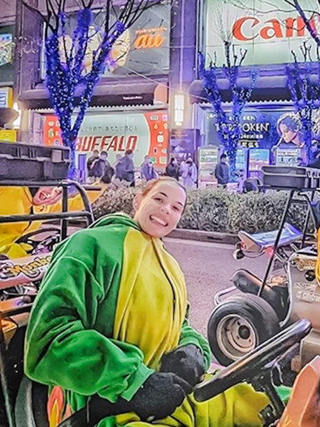 People in costume drive go-karts on a brightly lit street in Tokyo at night.