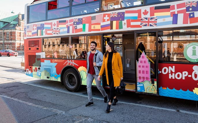 Hop-On Hop-Off bus with international flags, passengers exiting in a city setting.