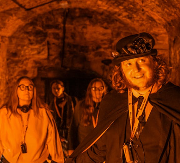 Tour guide leading Edinburgh Ghost Tour in underground vaults.
