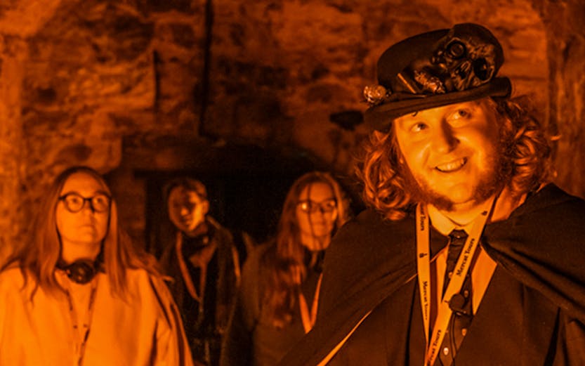 Tour guide leading Edinburgh Ghost Tour in underground vaults.