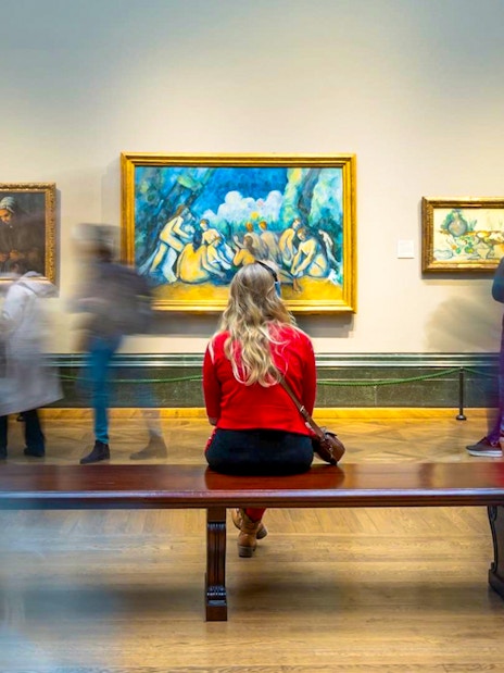 Woman sitting on bench viewing artwork at National Gallery guided tour.