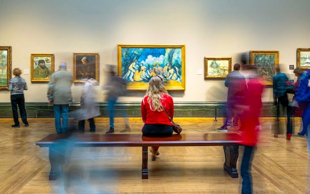 Woman sitting on bench viewing artwork at National Gallery guided tour.
