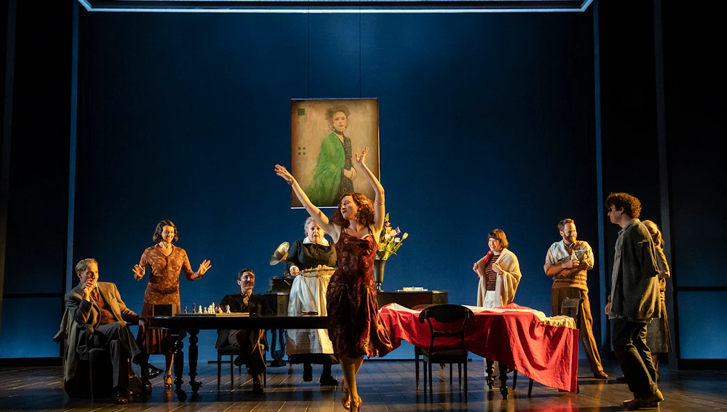 Theater scene from Leopoldstadt with actors around a table and a woman dancing.