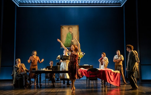 Theater scene from Leopoldstadt with actors around a table and a woman dancing.