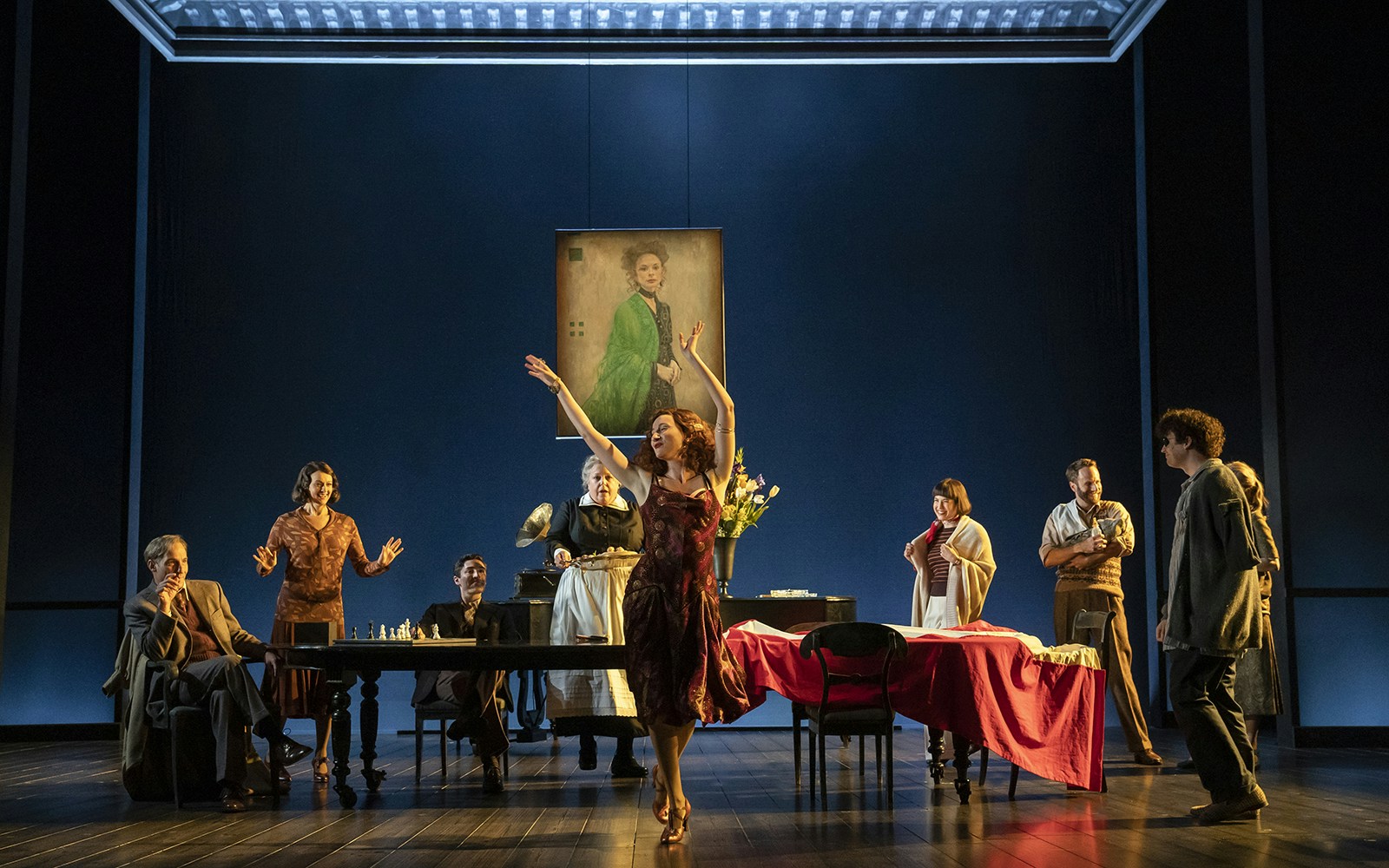 Theater scene from Leopoldstadt with actors around a table and a woman dancing.