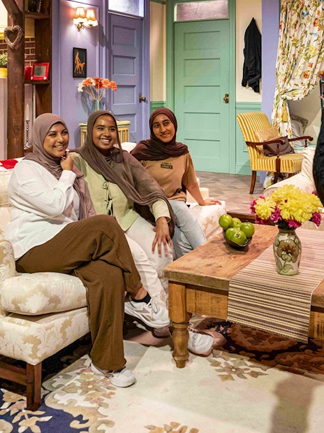 Visitors posing on the iconic FRIENDS™ set couch with kitchen backdrop.