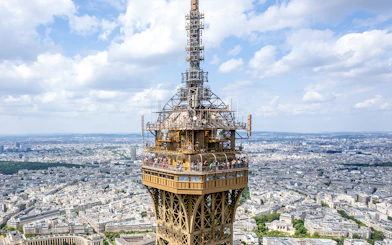 Eiffel Tower summit view with tourists on the observation deck, Paris skyline in background.