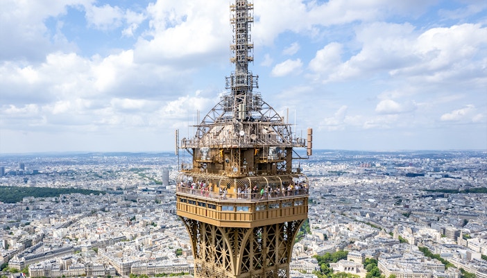 Eiffel Tower summit view with tourists on the observation deck, Paris cityscape in background.