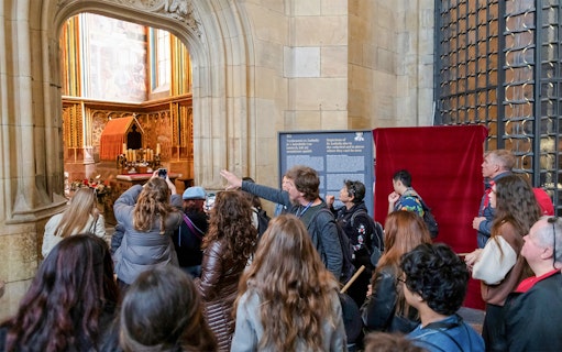 Tour group exploring Prague Castle interior with guide explaining historical details.