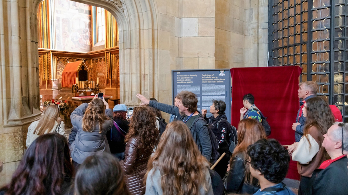 Tour group exploring Prague Castle interior with guide explaining historical details.