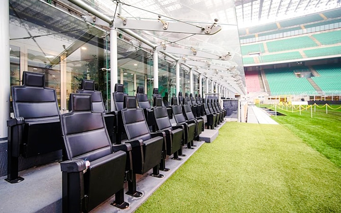Players' dugout at San Siro Stadium with black seats and view of the field.
