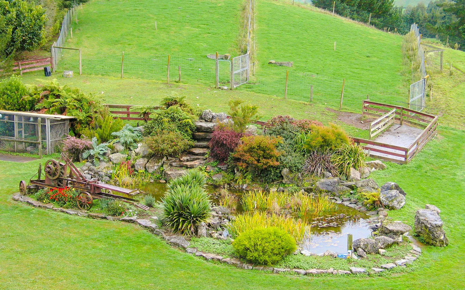 Altura Gardens in Waitomo featuring a pond surrounded by lush greenery and rustic stone steps.