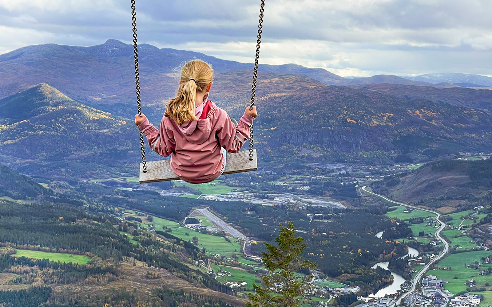 Girl swinging over Voss village with mountain and valley view.