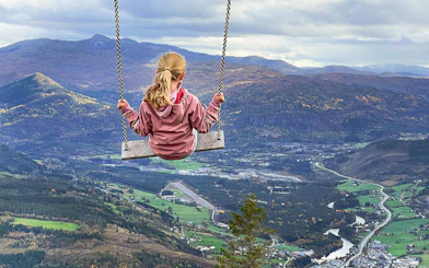 Girl swinging over Voss village with mountain and valley view.