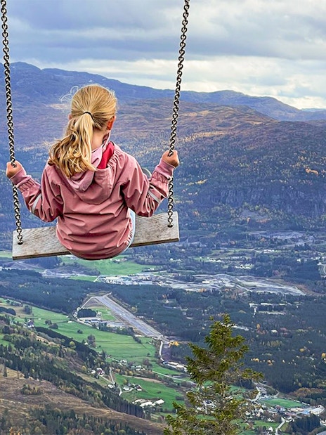 Girl swinging over Voss village with mountain and valley view.