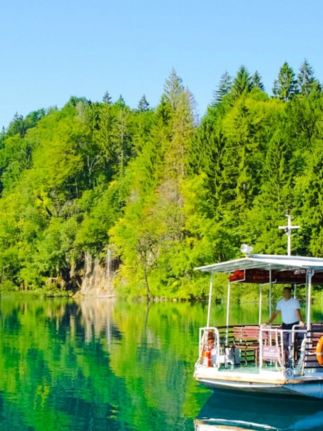 Boat on clear lake surrounded by lush forest at Plitvice Lakes National Park.