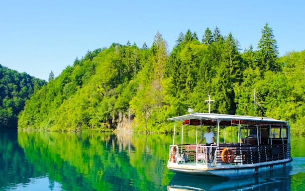 Boat on clear lake surrounded by lush forest at Plitvice Lakes National Park.