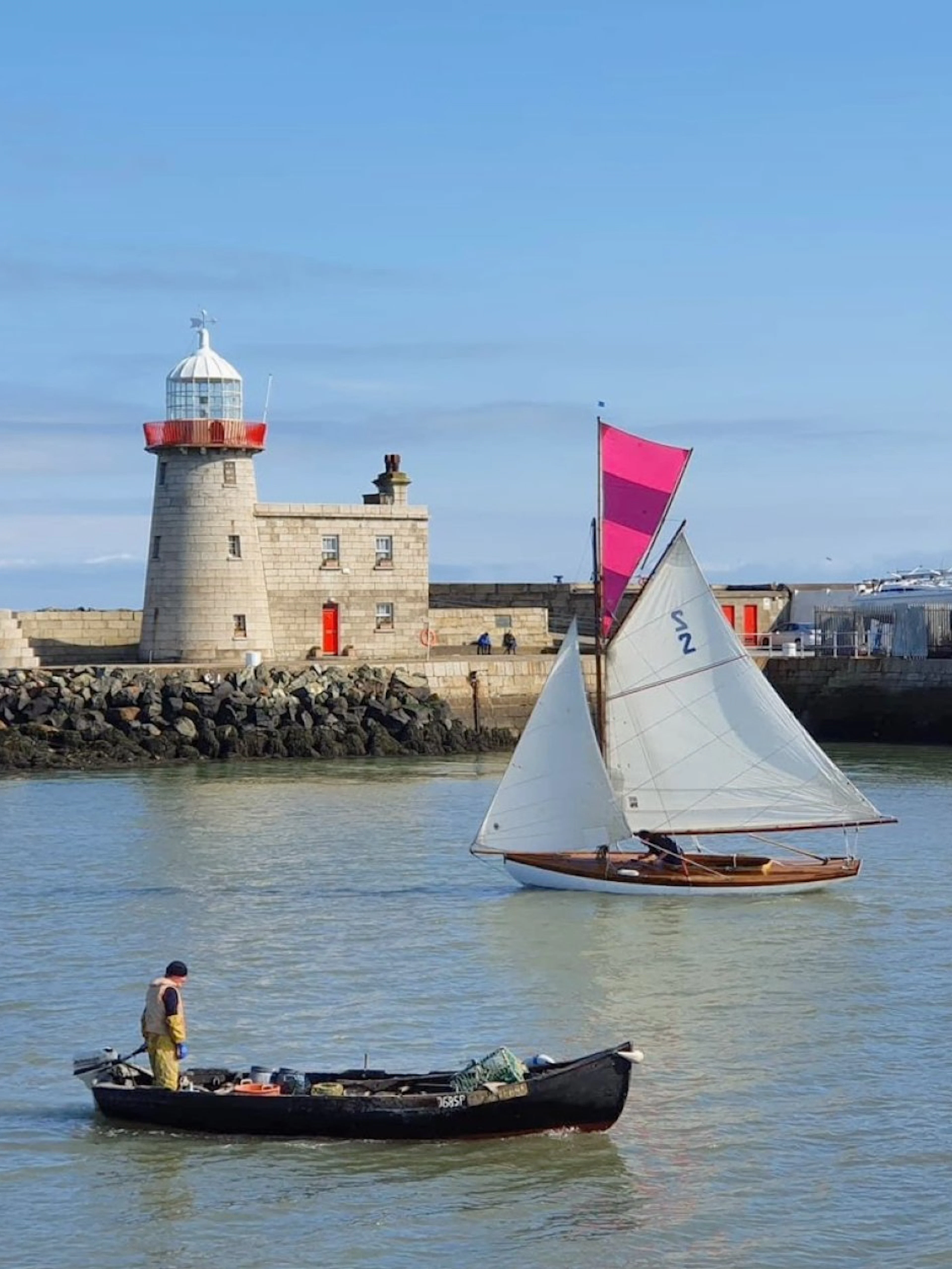 Sailboat and fishing boat near Howth Harbour lighthouse, Dublin.