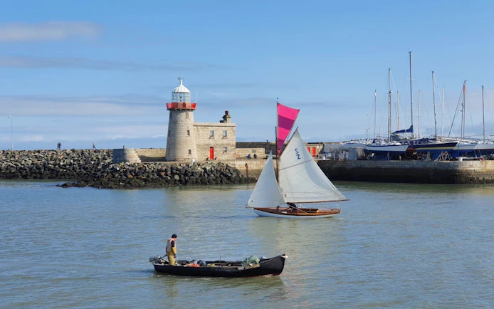Sailboat and fishing boat near Howth Harbour lighthouse, Dublin.