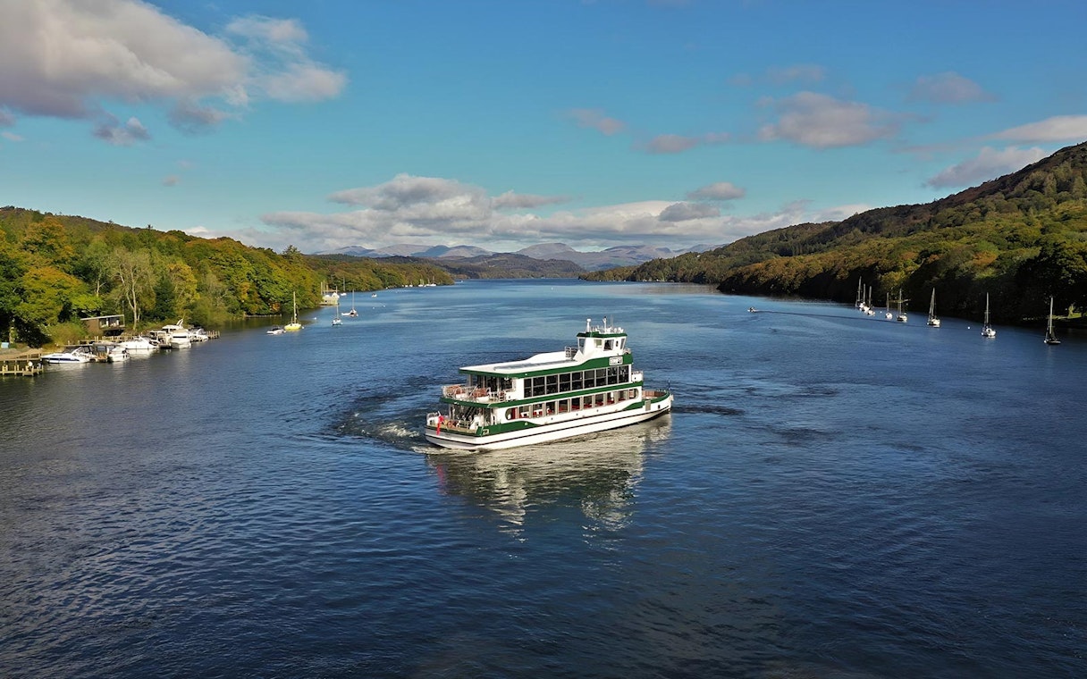 Cruise boat on Lake District waters with scenic hills, part of a day tour from London.